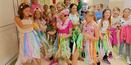 Powiększ grafikę: Kolorowo przebrane dzieci z klasy młodszych wraz ze swoimi trenerkami tańczą na korytarzu szkoły.